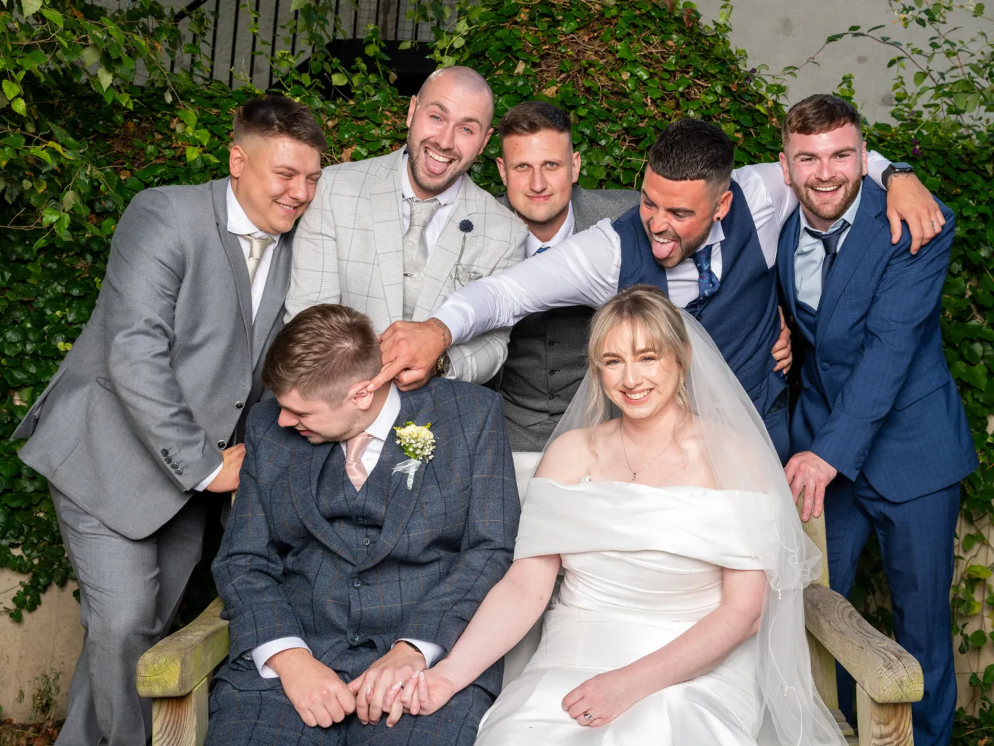 Bride and groom sitting on a bench while the grooms men pester the groom