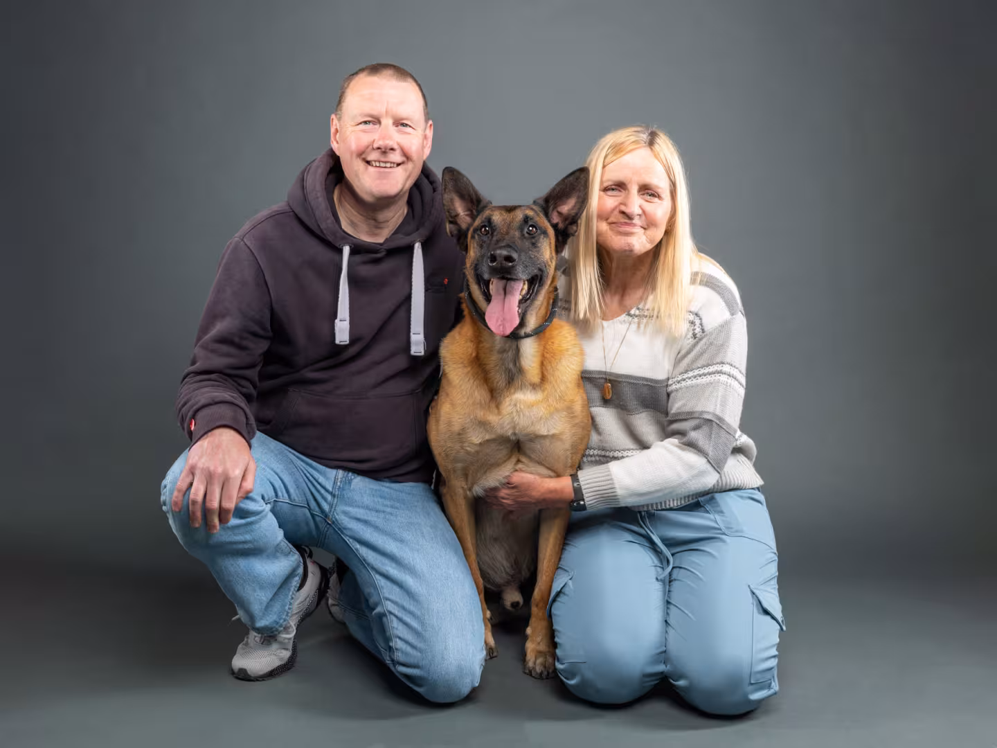 Man and woman crouching with a dog in the middle