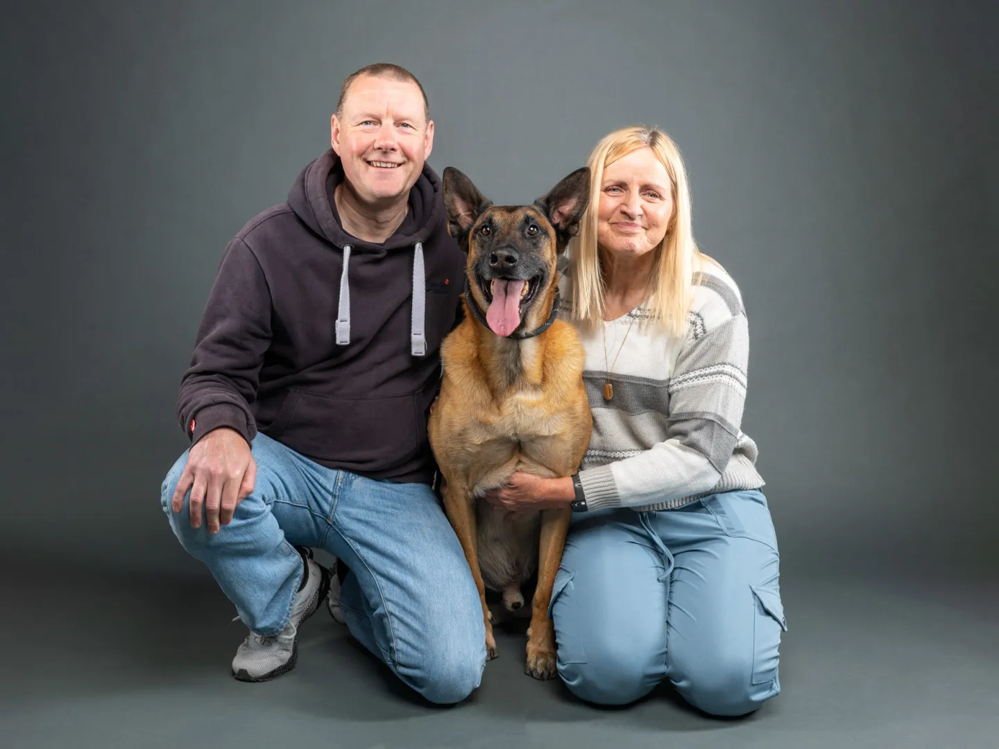 Man and woman crouching with a dog in the middle