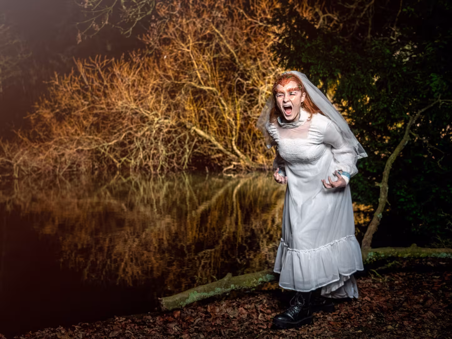 Woman in wedding dress standing at a lake at night screaming